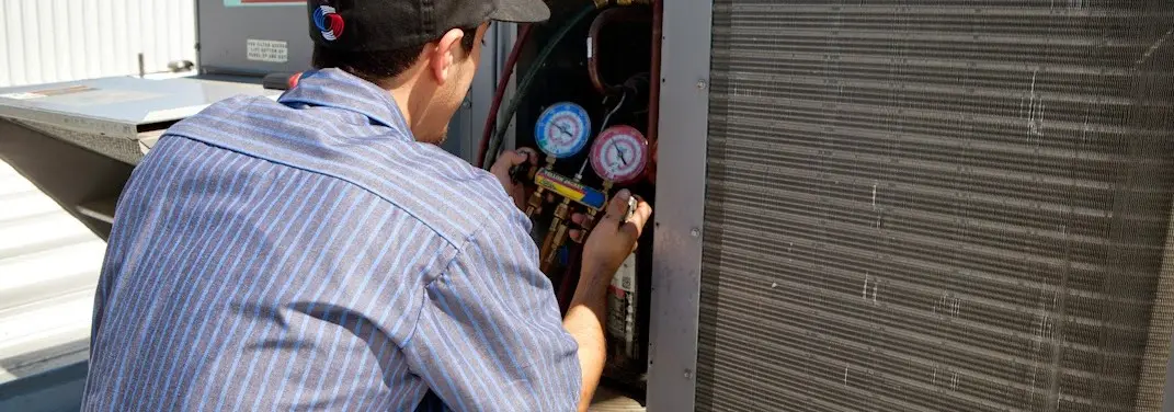 HVAC technician servicing a condenser unit in August